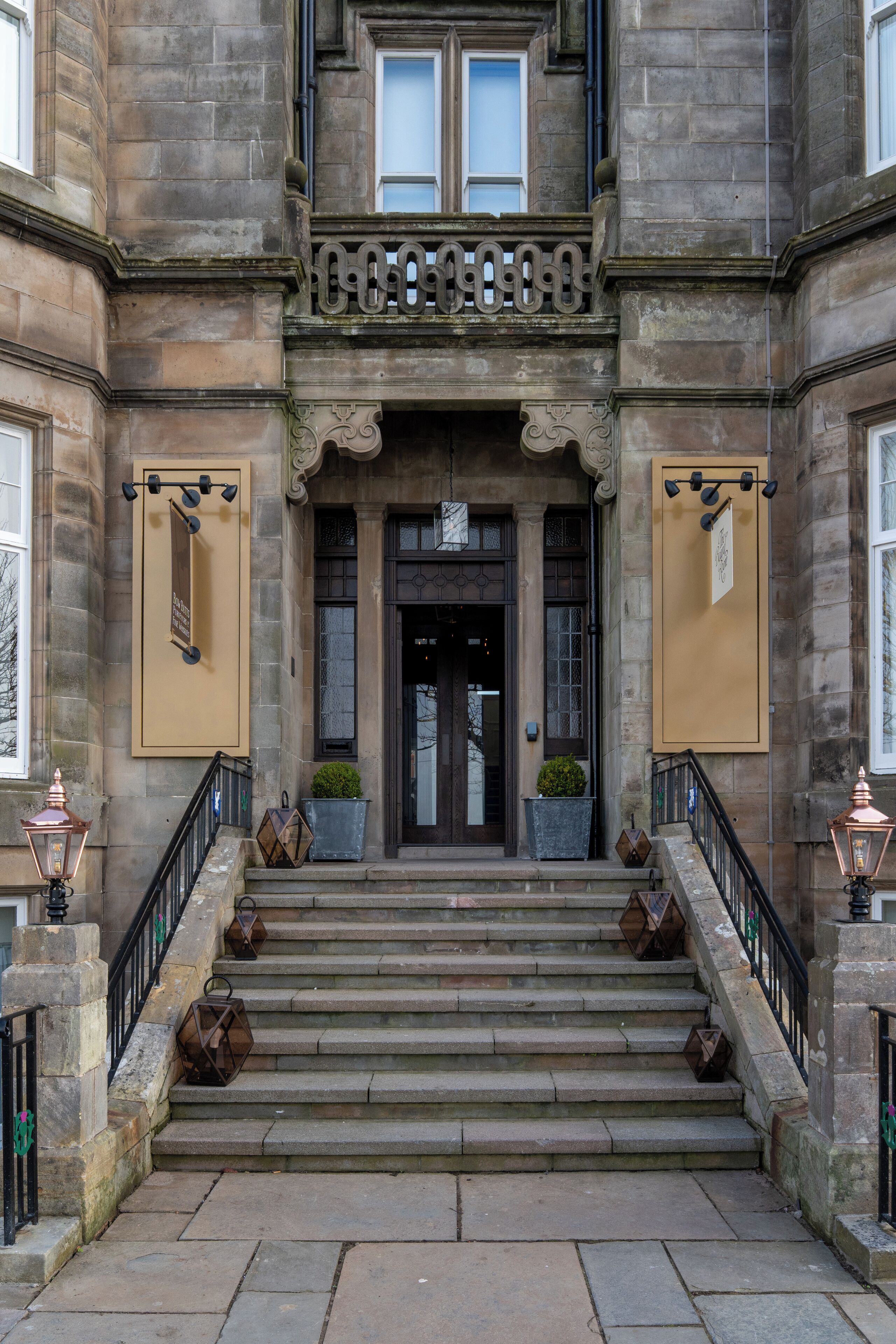 A stone building with a grand entrance, a staircase, and two potted plants on the steps.