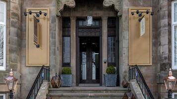 A stone building with a grand entrance, a staircase, and two potted plants on the steps.