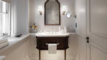 Une salle de bain avec un sol en marbre, un meuble-lavabo en bois, un grand miroir et deux appliques murales.