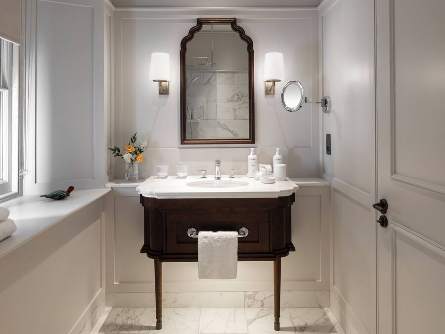Une salle de bain avec un sol en marbre, un meuble-lavabo en bois, un grand miroir et deux appliques murales.