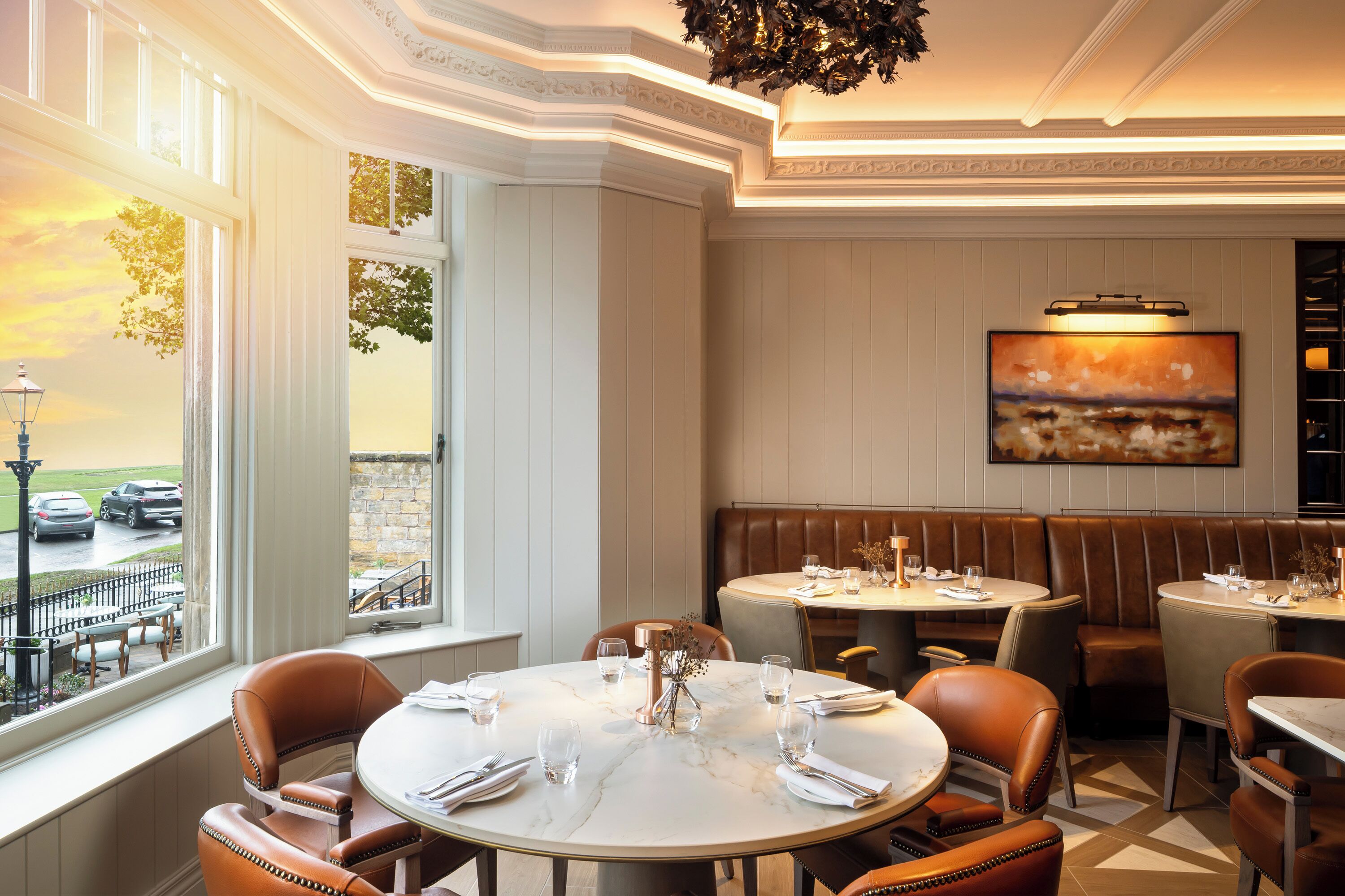 Un restaurante con mesas redondas, asientos de cuero y un cuadro grande en la pared.