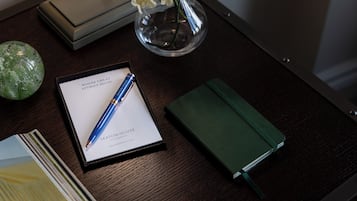 Un escritorio con una libreta, un bolígrafo, un florero de vidrio con flores y un objeto decorativo.