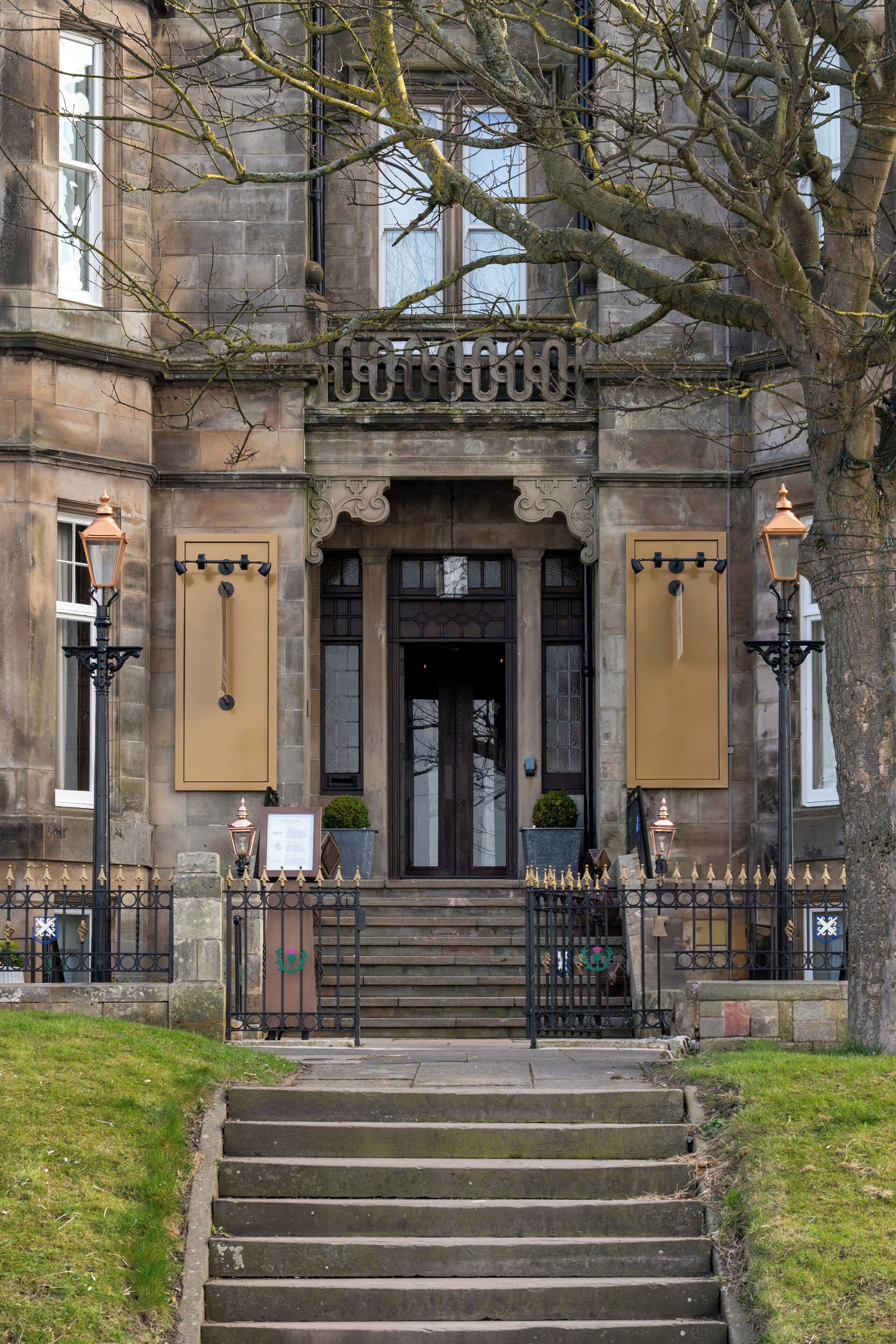 Un edificio histórico con fachada de piedra, una entrada central con puerta negra y un cartel sobre la puerta.