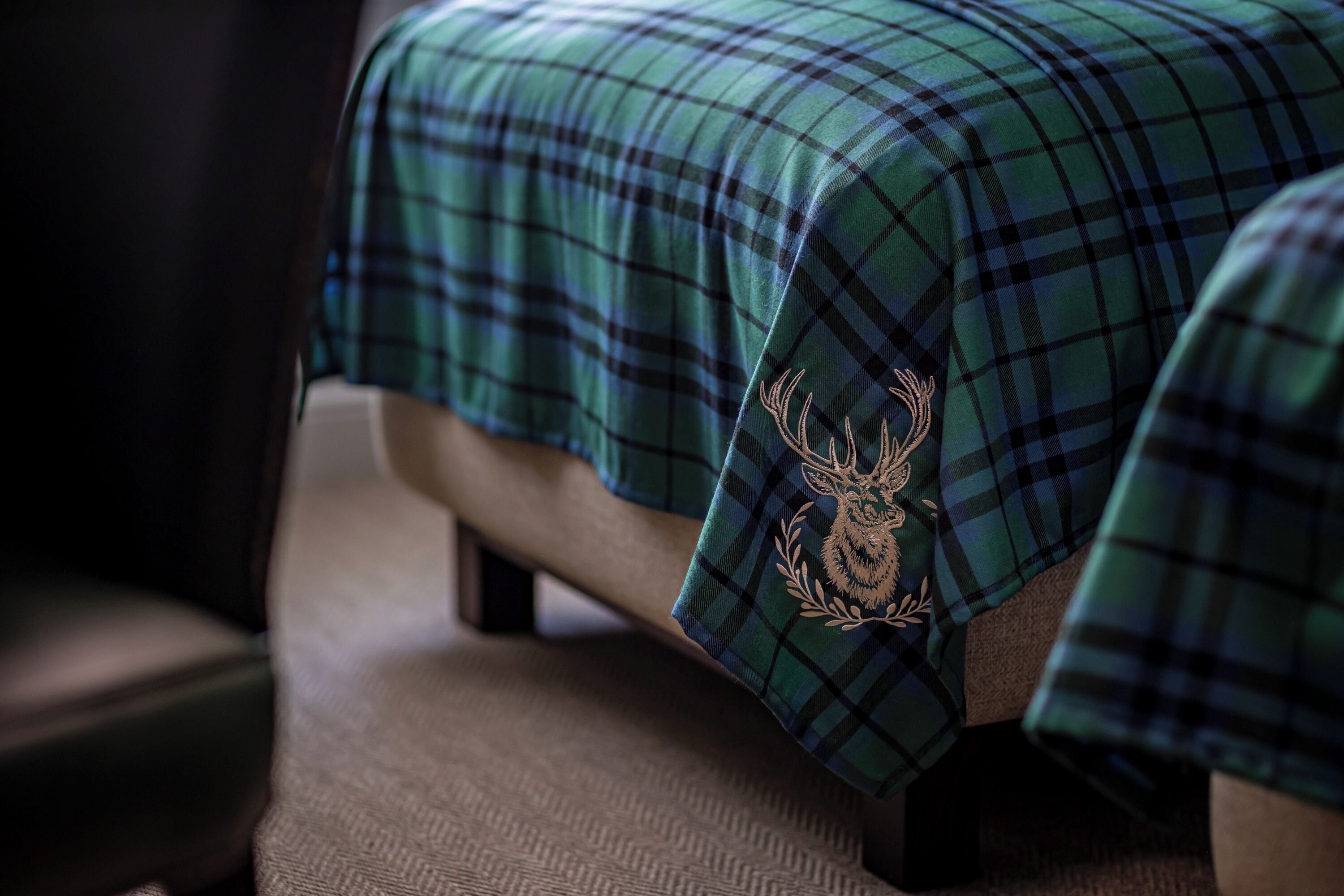A bed with a plaid blanket featuring a deer emblem.