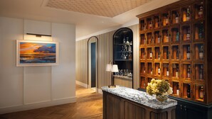 Een bar met een houten kast vol flessen, een marmeren aanrecht en een lijst met een schilderij aan de muur.