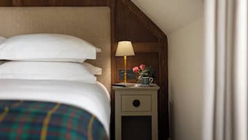 A neatly made bed with white linens and a plaid blanket, a bedside table with a lamp, a cup, and a vase with flowers, and a wooden panel wall.