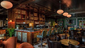 Een bar met zitplaatsen, een toog en flessen op planken.
