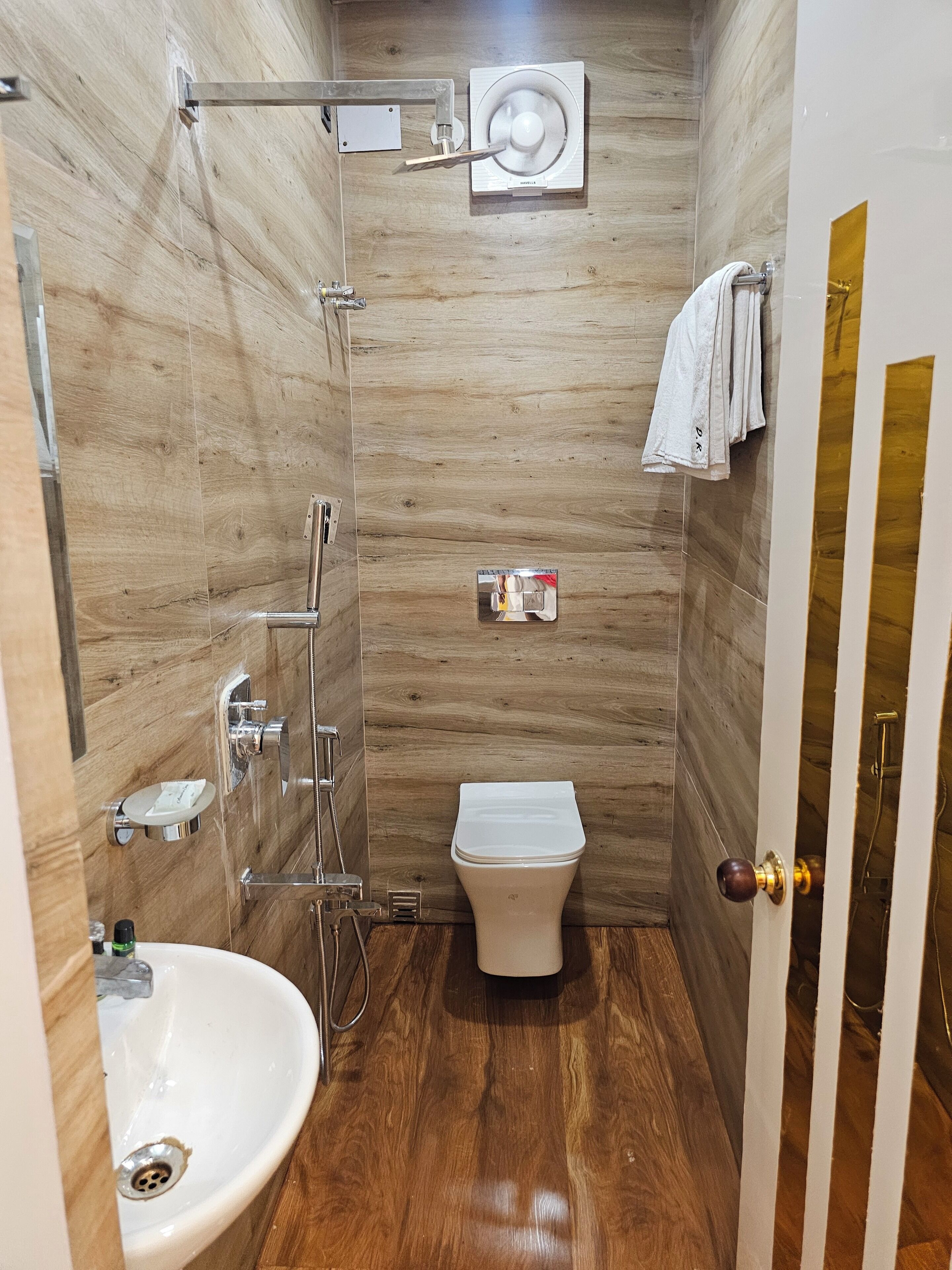 A small, modern bathroom with a wooden floor, a white toilet, a sink, and a shower.