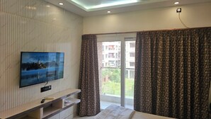 Un dormitorio con cama, televisor montado en la pared, ventilador de techo y ventana con cortinas.