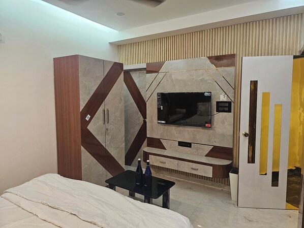 A bedroom with a bed, a TV mounted on the wall, a wardrobe, and a door with a unique design. - LUXE LAGOON (Barasat)