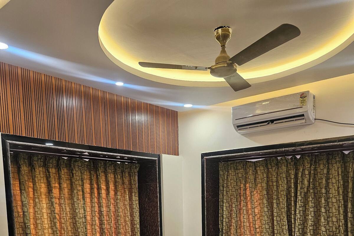 A modern hotel room with a large bed, a sofa, a ceiling fan, and an air conditioning unit.