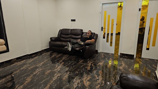 A room with a black leather sofa, a marble floor, and a door with yellow tape.
