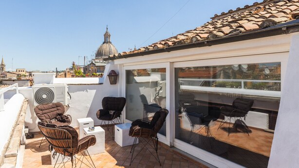 A rooftop terrace with outdoor seating, a large window, and a view of a cityscape including a church.