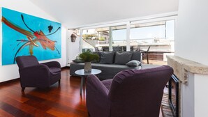 A modern living room with a large abstract painting, a grey sofa, two purple armchairs, and a small round table with a plant.