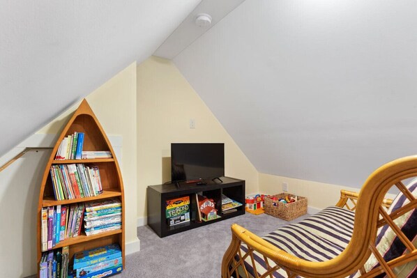 A room with a bookshelf, a television, a wicker chair, and a small table with toys.