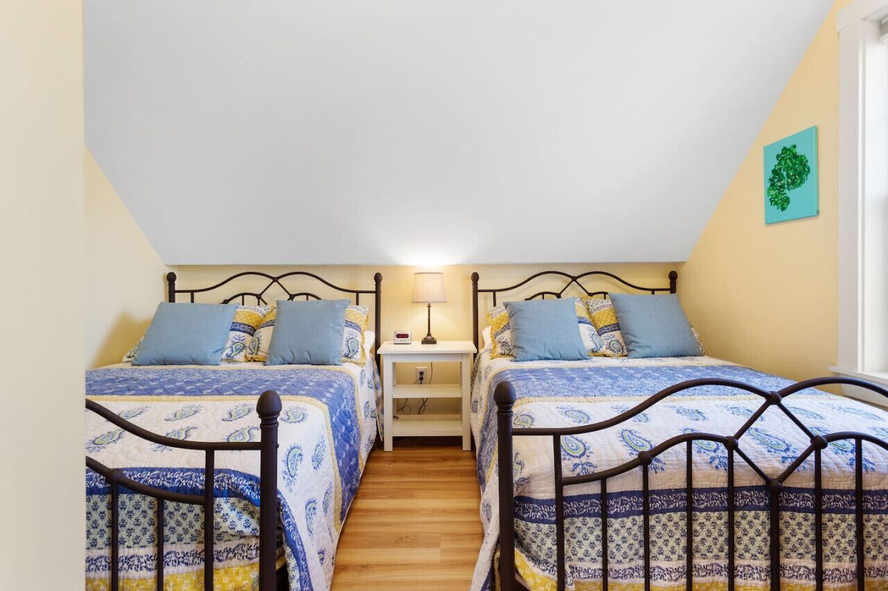 A bedroom with two beds, a nightstand, and a wall-mounted lamp.