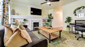 A living room with a sofa, coffee table, fireplace, television, ceiling fan, and potted plants. - Lemonade Lodge (Oklahoma City)