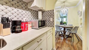 A kitchen with a microwave, coffee maker, and utensils, leading to a dining area with a chandelier. - Lemonade Lodge (Oklahoma City)