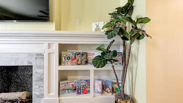 Ein Wohnzimmer mit Kamin, einem darüber hängenden Fernseher und einem Bücherregal mit Gesellschaftsspielen.