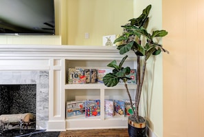 A living room with a fireplace, a television mounted above it, and a bookshelf with board games.