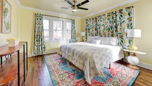 A bedroom with a bed, a ceiling fan, a window with curtains, a bedside lamp, and a rug. - Lemonade Lodge (Oklahoma City)