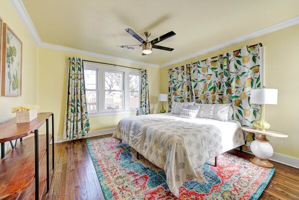 Un dormitorio con cama, ventilador de techo, ventana con cortinas, lámpara de noche y alfombra.