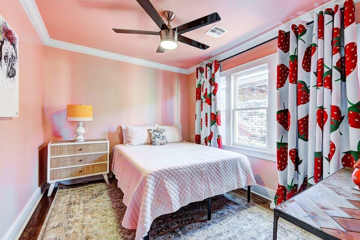 A bedroom with a bed, a ceiling fan, a nightstand with a lamp, a window with curtains, and a rug.