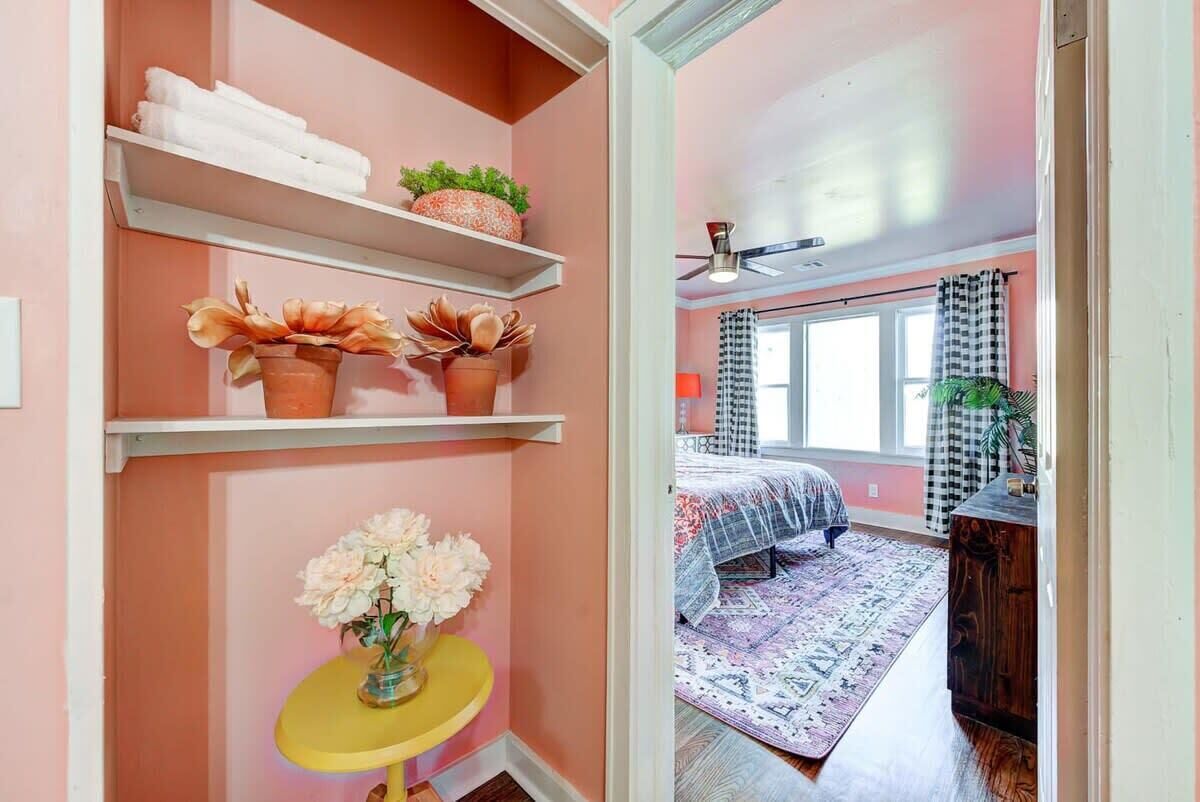 Un dormitorio con cama, alfombra, ventana con cortinas y estante con toallas y plantas.