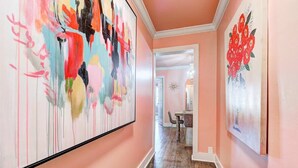 A hallway with pink walls, wooden flooring, and two large abstract paintings. - Strawberry Lodge-adorable duplex in central NW OKC (Oklahoma City)