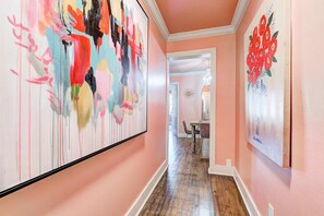 Un pasillo con paredes rosas, piso de madera y dos grandes cuadros abstractos.