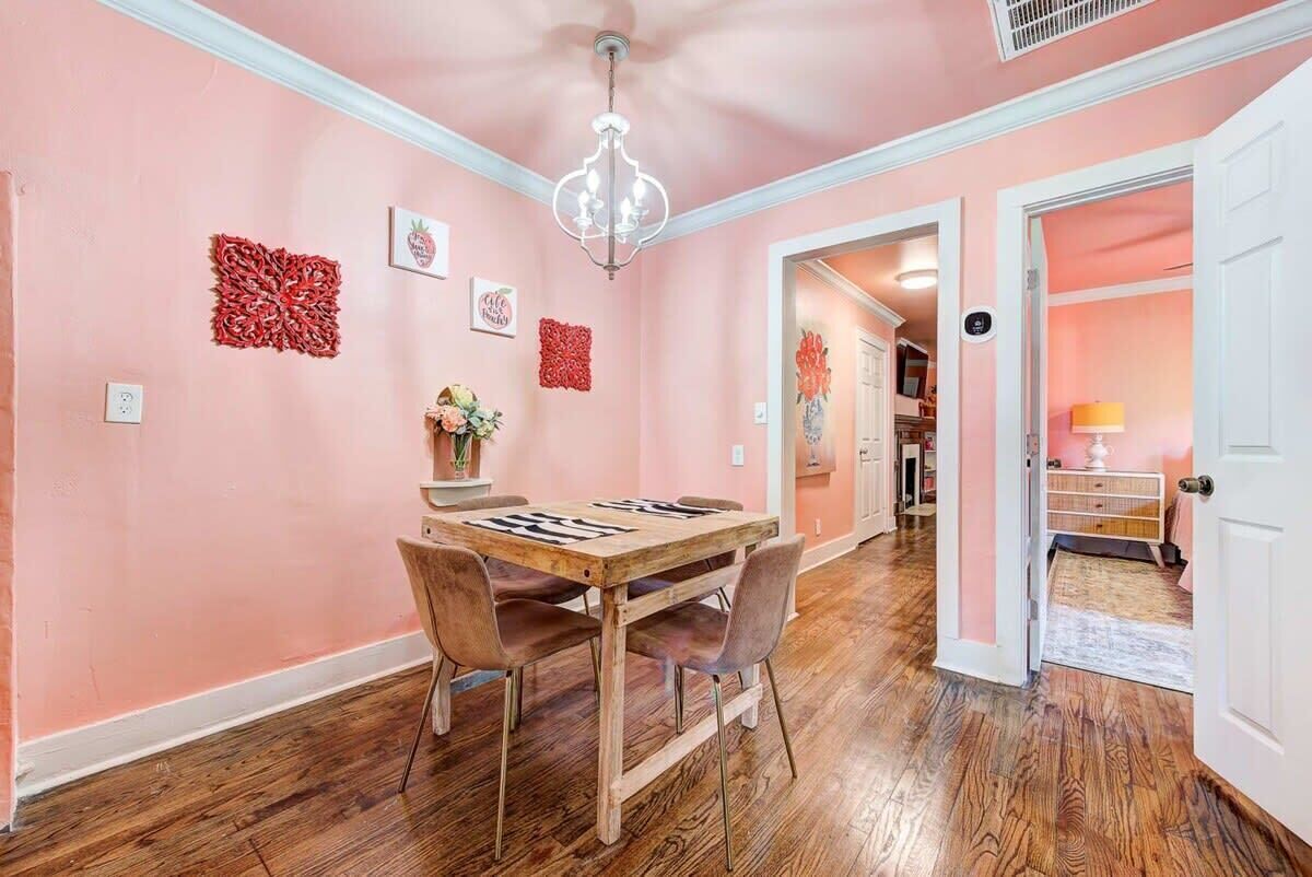 A dining area with a wooden table and chairs, pink walls, and a chandelier.