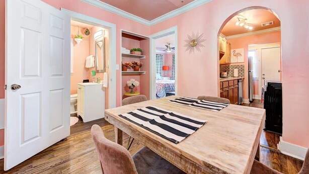 A dining area with a wooden table and striped placemats, pink walls, and a white door. - Strawberry Lodge-adorable duplex in central NW OKC (Oklahoma City)