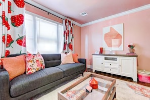 Una sala de estar con un sofá, una mesa de centro, un armario blanco y una ventana con cortinas.