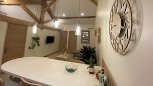 A kitchen with a large island, pendant lights, wooden beams, a clock, and a TV.