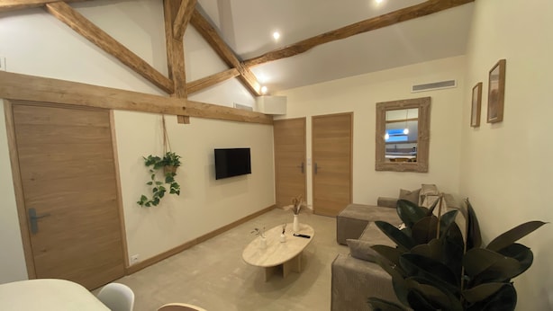A room with a wooden ceiling, a television mounted on the wall, a round table, and a sofa.