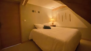 A bedroom with a sloped ceiling, a bed with white bedding, a bedside lamp, and a small wall-mounted shelf.
