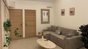 A living room with a wooden door, a mirror, a sofa, and a table with a vase.