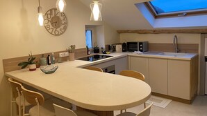 A modern kitchen with a central island, wooden beams, pendant lighting, and a skylight.
