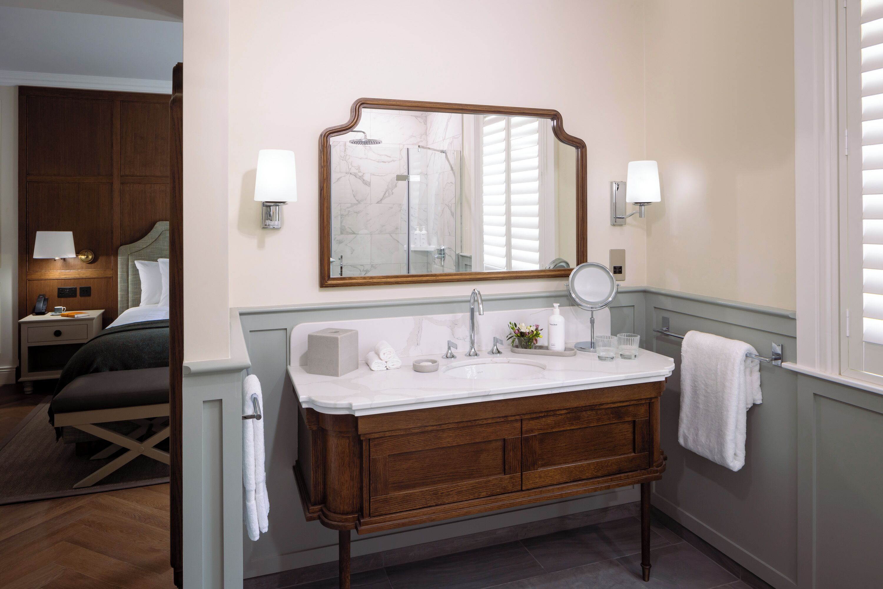 A bathroom with a wooden vanity, a large mirror, and a sink. There is a towel rack with a towel hanging on it.