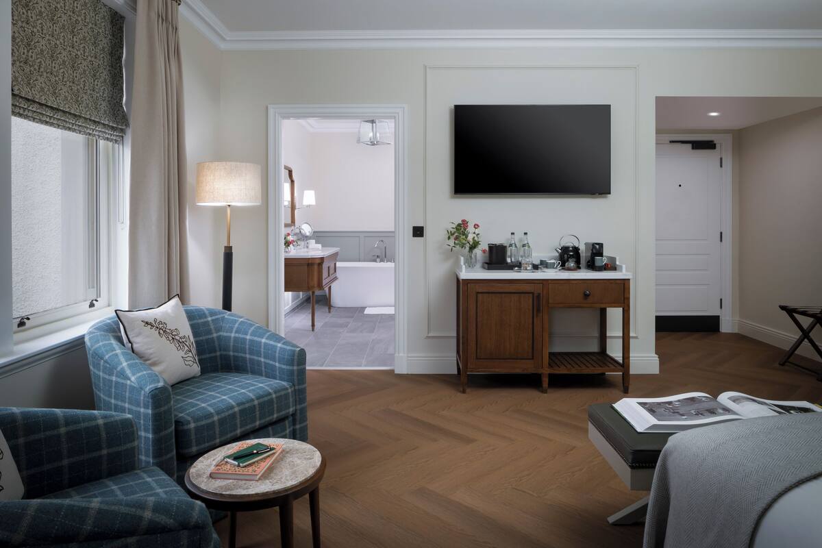A modern living room with a sofa, a small round table, a coffee table, a TV mounted on the wall, and a view into the adjacent bathroom.