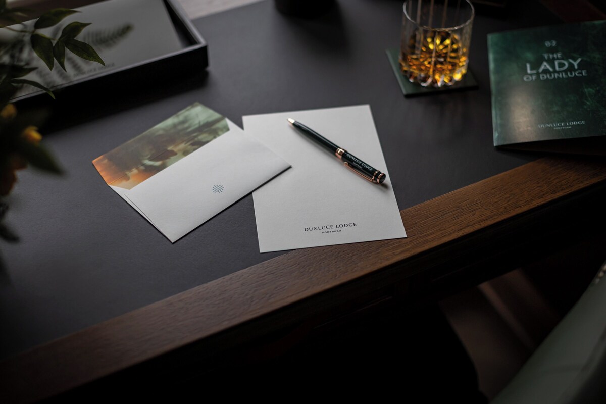 Un bureau en bois, sur lequel se trouvent un stylo, un livre intitulé « La Dame de Bunluke » et un verre contenant un liquide de couleur ambrée.