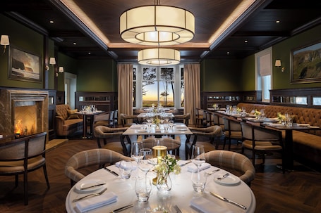 A formal dining room with multiple tables set for service, a fireplace, and a view of the outdoors.