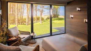Une chambre moderne avec une grande fenêtre, des meubles en osier, une petite table avec un plateau et un lit.