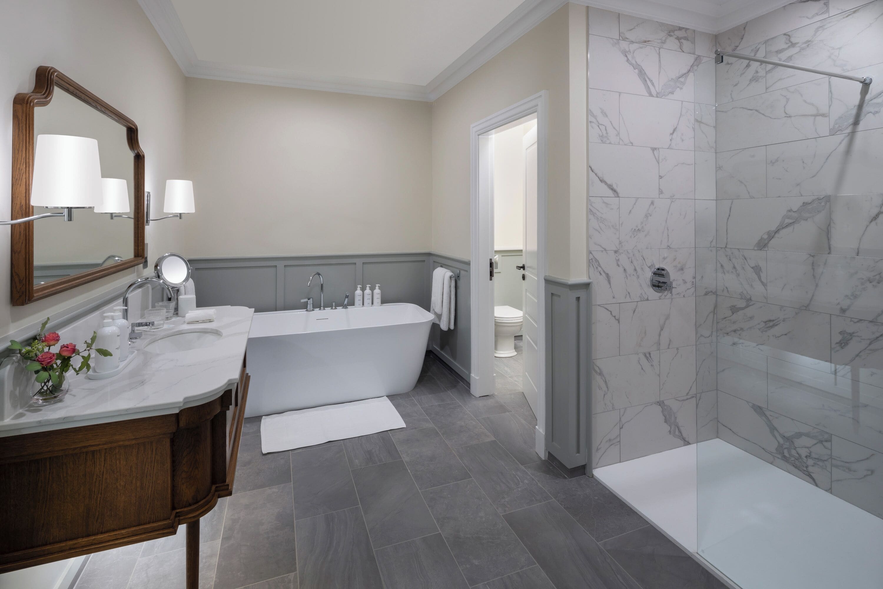 Un baño moderno con tocador doble lavamanos, bañera independiente y ducha a ras de suelo con baldosas de mármol.