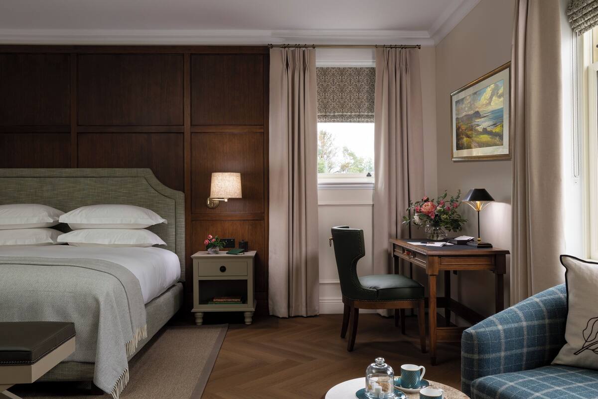 A hotel room with a large bed, a desk with a lamp, a chair, and a couch.