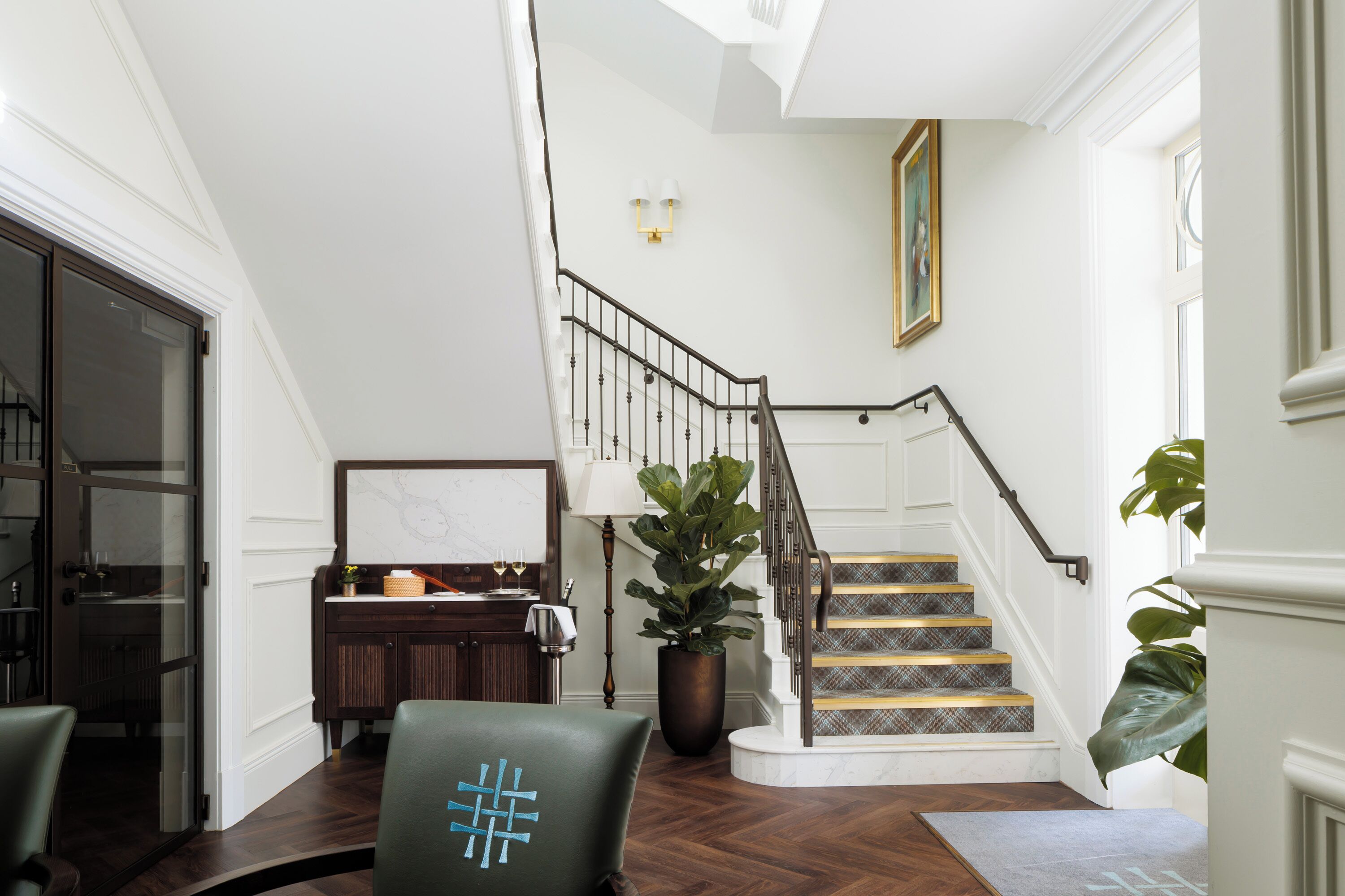 A staircase with a patterned carpet leading to a landing with a marble wall and a framed painting.