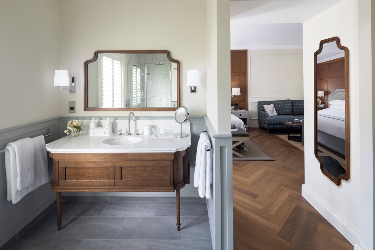 A modern bathroom with a wooden vanity, two sinks, a large mirror, and a shower.