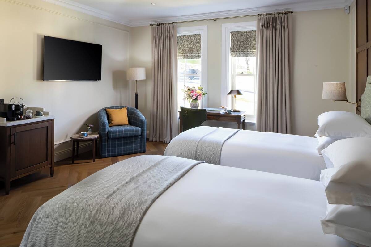 A hotel room with two beds, a desk, a chair, a TV, and a window with curtains.