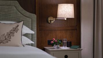 A neatly made bed with a pillow and a bedside table with a lamp, a vase with flowers, and a book.