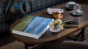 Un livre intitulé « L’histoire du Manhattan » est posé sur une table en bois, accompagné d’une tasse, d’une soucoupe et d’un petit vase avec des fleurs.